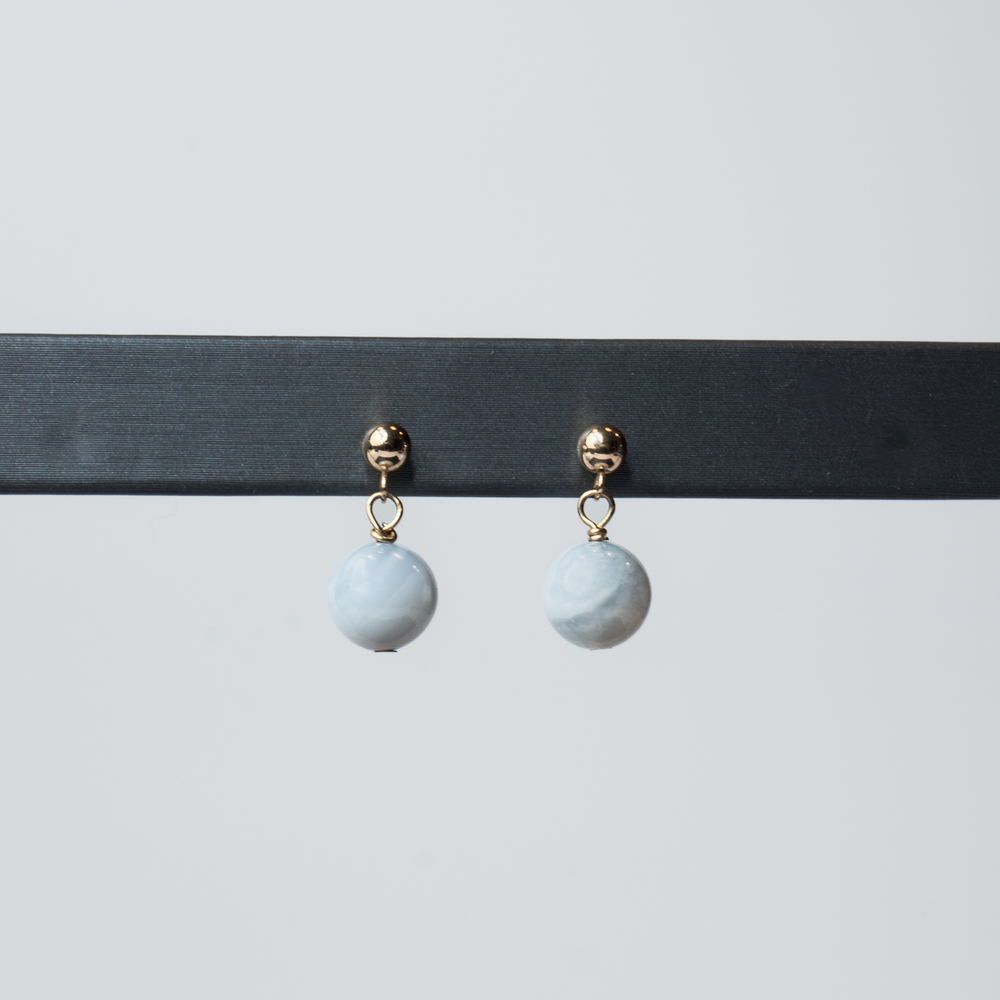 
                      
                        The Agate Boule Earrings by Pear. are showcased on a black horizontal bar, presenting their elegant design of gold and marble-patterned drop earrings. Each earring is adorned with a round agate boule bead suspended from a 14K gold ball stud against a plain white background.
                      
                    