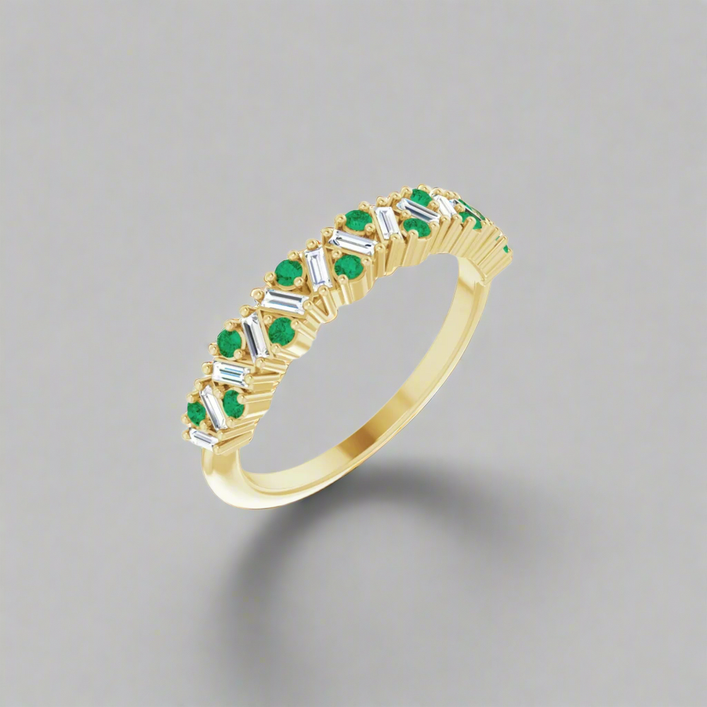 Introducing the Eloise Gemstone and Diamond Scattered Ring by Pear: a luxurious piece featuring a gold band elegantly embellished with an alternating pattern of small emerald gemstones and baguette-cut diamonds, strikingly presented against a plain grey backdrop.