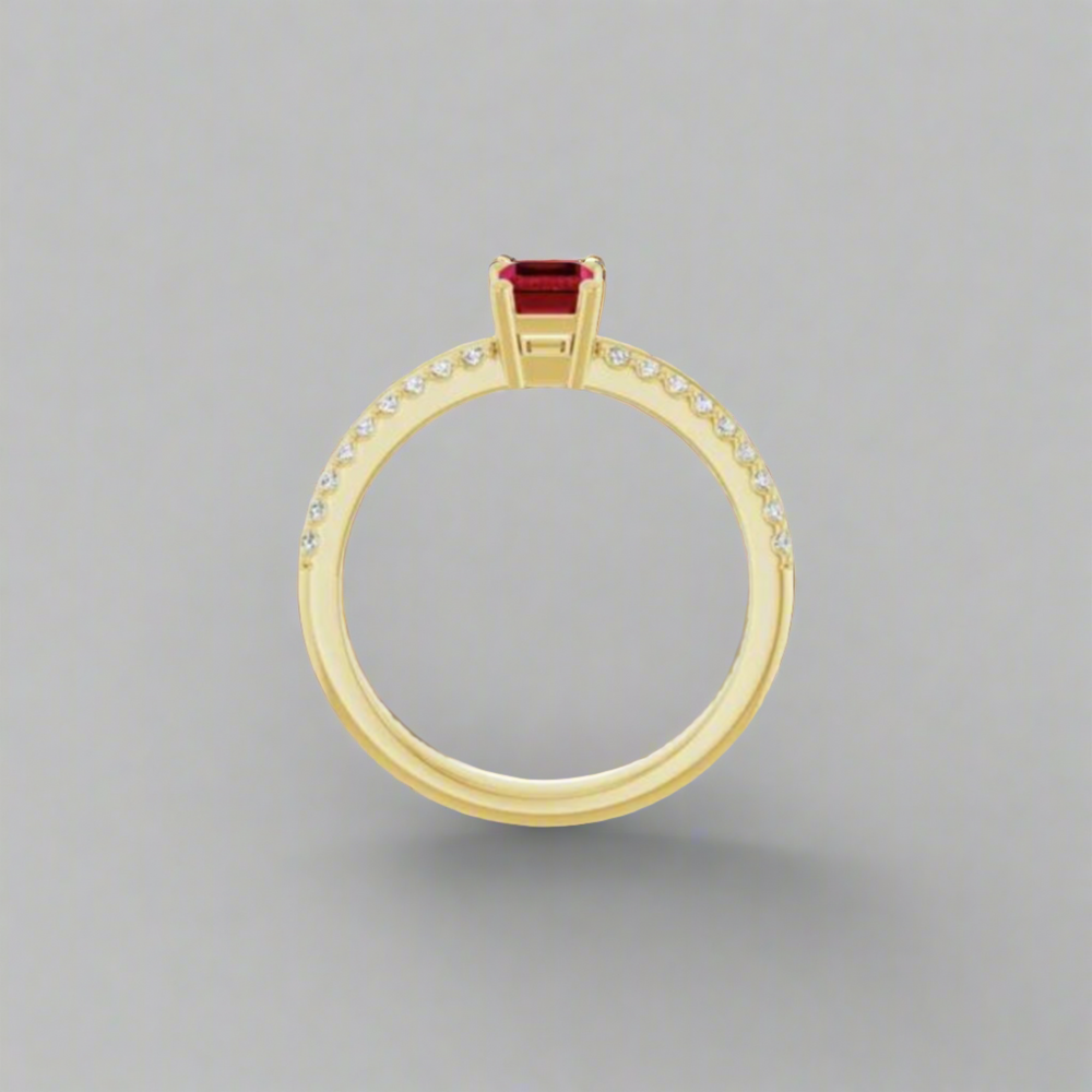 The Pear Elyse Ruby Ring is showcased vertically, featuring a step cut ruby at its pinnacle. The gold band on the upper half sparkles with 18 full cut diamonds, all set against a simple grey background.