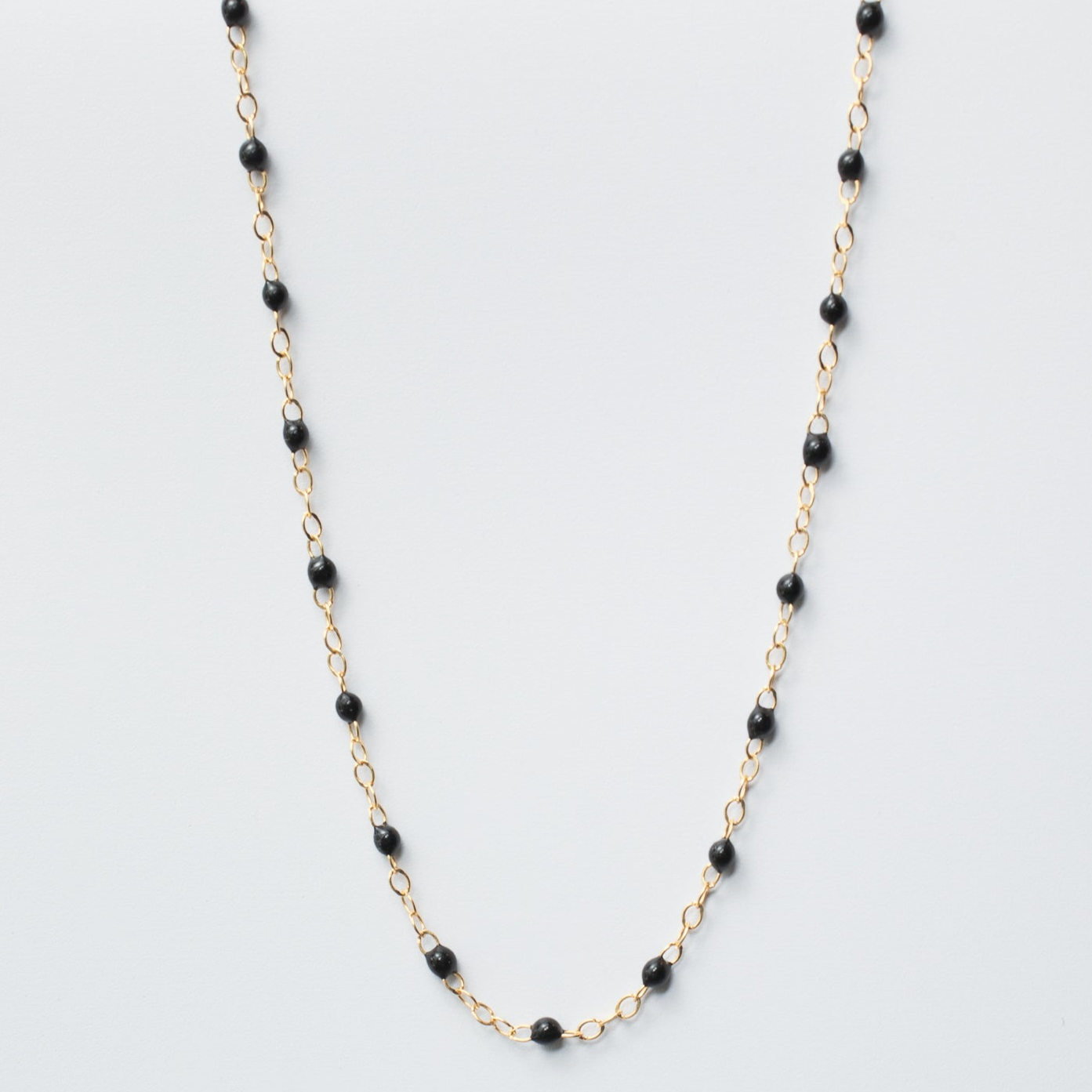 A delicate gold chain necklace with small round black enamel beads evenly spaced throughout. This simple yet elegant design, reminiscent of the Pear Enamel Satellite Bracelet, creates a stylish and versatile accessory. The necklace is displayed against a plain white background.