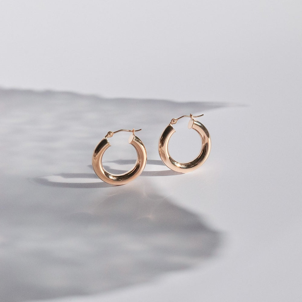 
                      
                        A pair of Pear's Mini Thick Hoops, crafted in 14K gold, are elegantly displayed on a pristine, white surface. The hoops are pictured with their clasps open, casting a delicate shadow to the left and creating a minimalist and sophisticated presentation ideal for everyday wear.
                      
                    