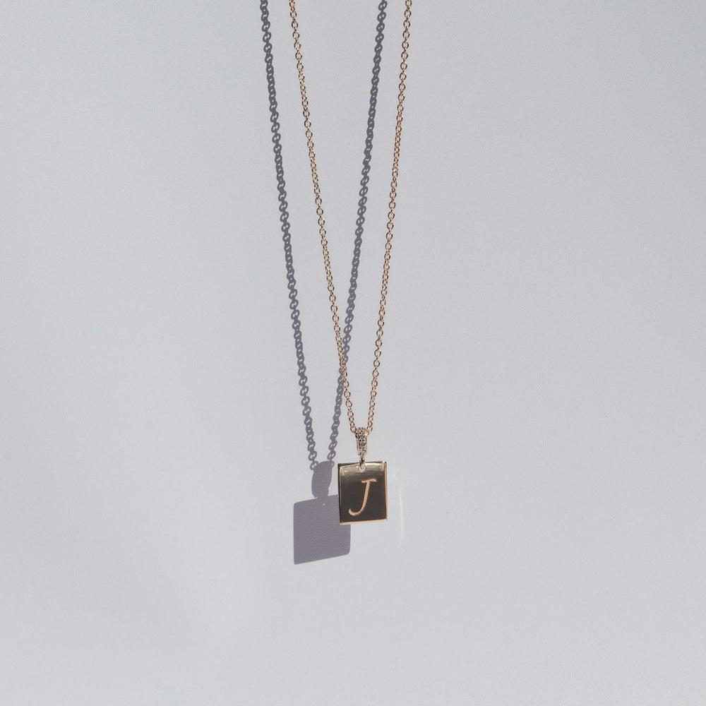 
                      
                        A delicate gold Diamond Cleo Initial Necklace by Pear, showcasing a rectangular pendant adorned with the letter "J" in cursive. The customizable pendant casts a subtle shadow against a light grey background, giving it a minimalist and elegant appearance.
                      
                    