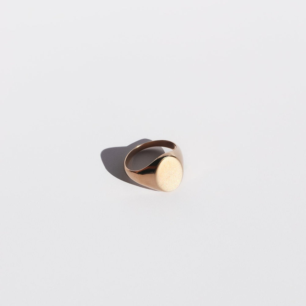 
                      
                        The Oval Signet Ring by Pear. is exhibited against a pristine, white backdrop, showcasing its minimalist design with a smooth oval face. A gentle shadow falls to the left of the ring, accentuating its sleek silhouette and polished gold finish.
                      
                    