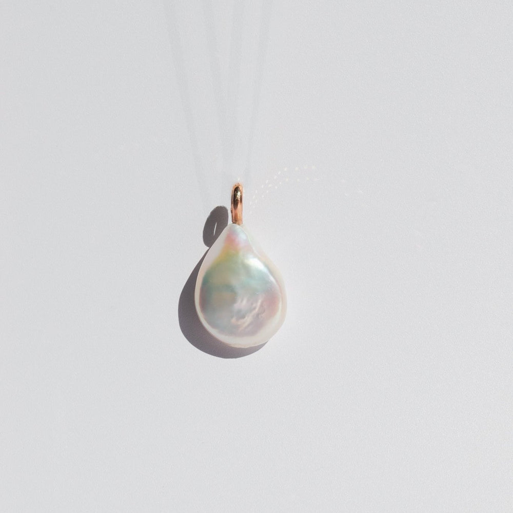 
                      
                        A close-up of the Baroque Pearl Necklace by Pear, featuring a teardrop-shaped baroque pearl pendant with a 14K yellow gold loop, hanging against a plain white background. The lustrous, iridescent surface of the pearl reflects light, revealing subtle hues of white, pink, and green. Various chain options are available for customization.
                      
                    