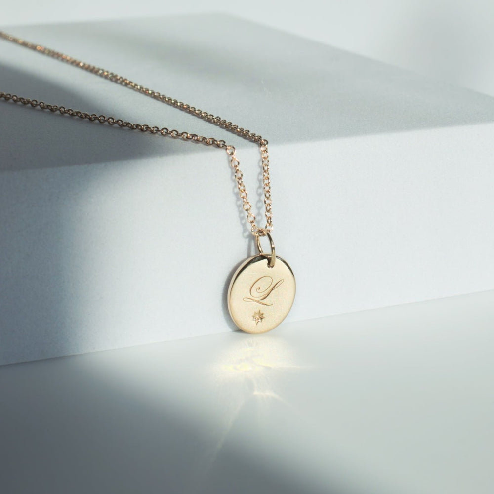 
                      
                        A gold Oval Engravable Necklace from Pear features a sophisticated round charm with an engraved letter "L" and a small star symbol. The adjustable cable chain delivers versatility, beautifully accentuated by a minimalist, light-colored background with soft shadows and reflections that highlight the pendant's elegant surface.
                      
                    