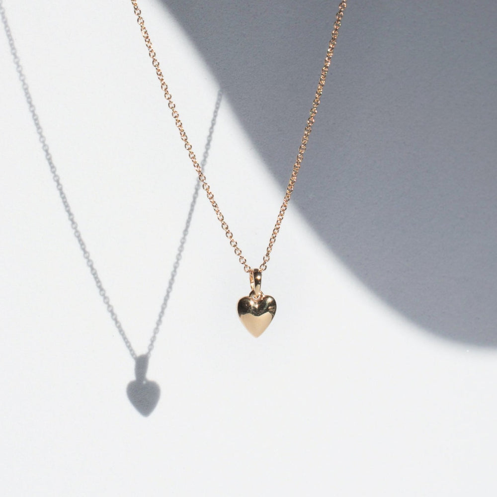 
                      
                        Image of Pear's Puffed Heart Necklace in gold, displayed on an adjustable cable chain and casting a shadow against a plain white background. The polished heart pendant has a shiny, reflective surface that enhances the minimalist and elegant aesthetic of this lightweight jewelry piece.
                      
                    