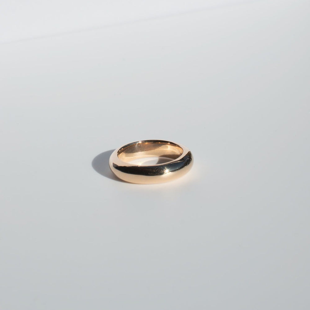 
                      
                        A shiny, solid gold band from Pear called the Heavy Band with a smooth, polished surface rests on a light gray background. The classic wedding band casts a subtle shadow, highlighting its elegant and simple design.
                      
                    