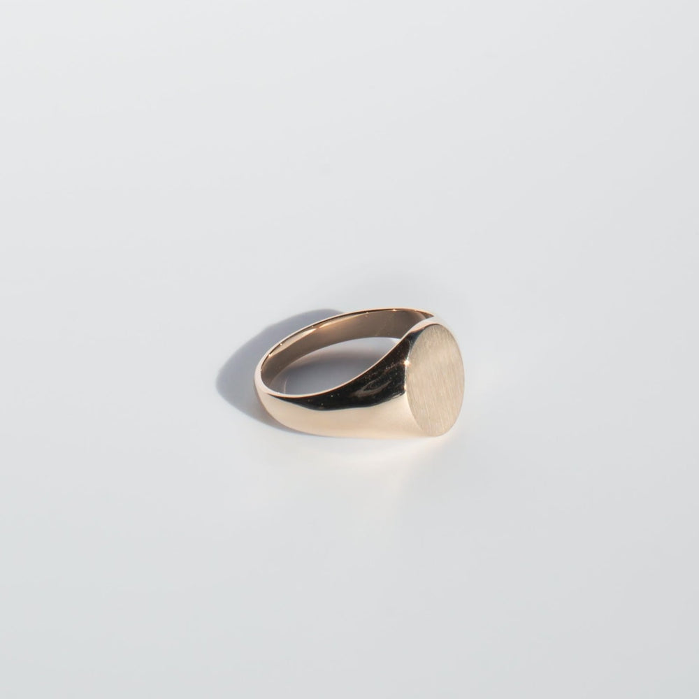 
                      
                        An Oval Signet Ring by Pear., crafted from minimalist solid gold, featuring a smooth, round, and unengraved top surface. The ring is photographed against a light grey background, enhancing its polished and elegant design.
                      
                    