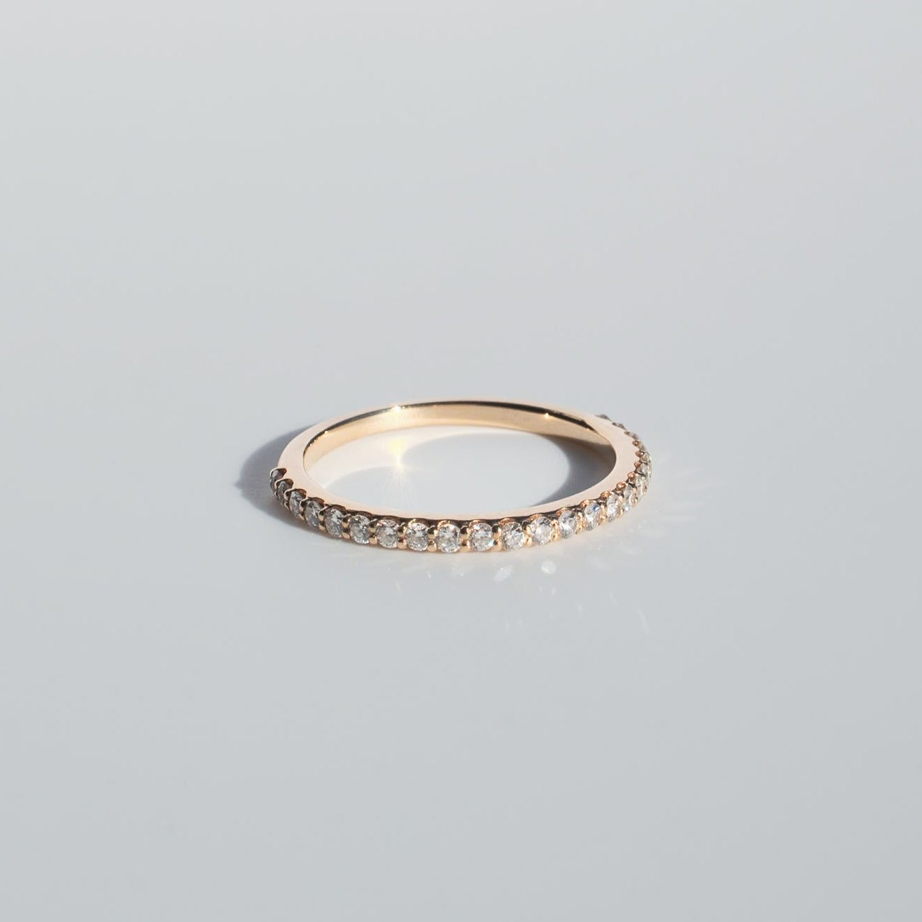 A delicate Diamond French Band from Pear., crafted from gold with a continuous series of small, sparkling diamonds, is displayed against a clean, light gray background. The ring's simple yet elegant design is highlighted by the radiant sparkle of the diamonds.