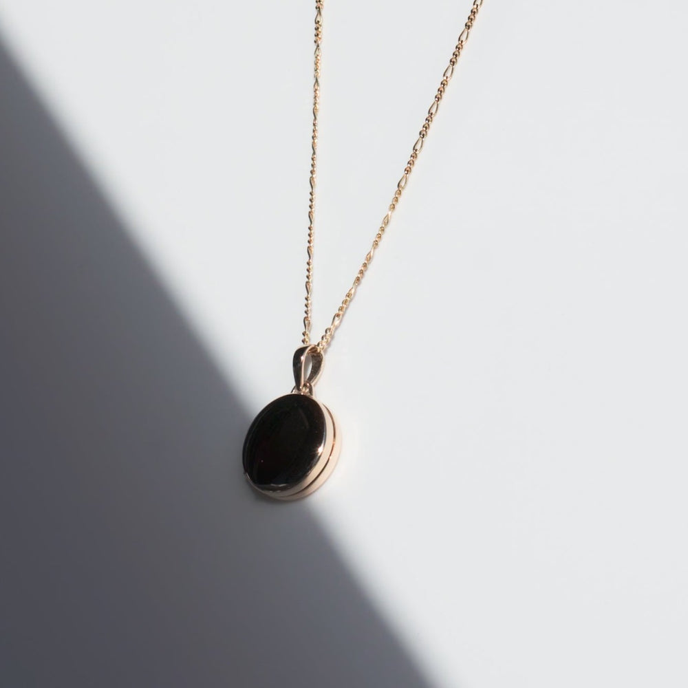 
                      
                        A 14K gold Round Locket by Pear is displayed against a light background. The delicately crafted piece, featuring a Figaro chain, casts a soft shadow, creating a diagonal light-and-shadow effect across the image.
                      
                    