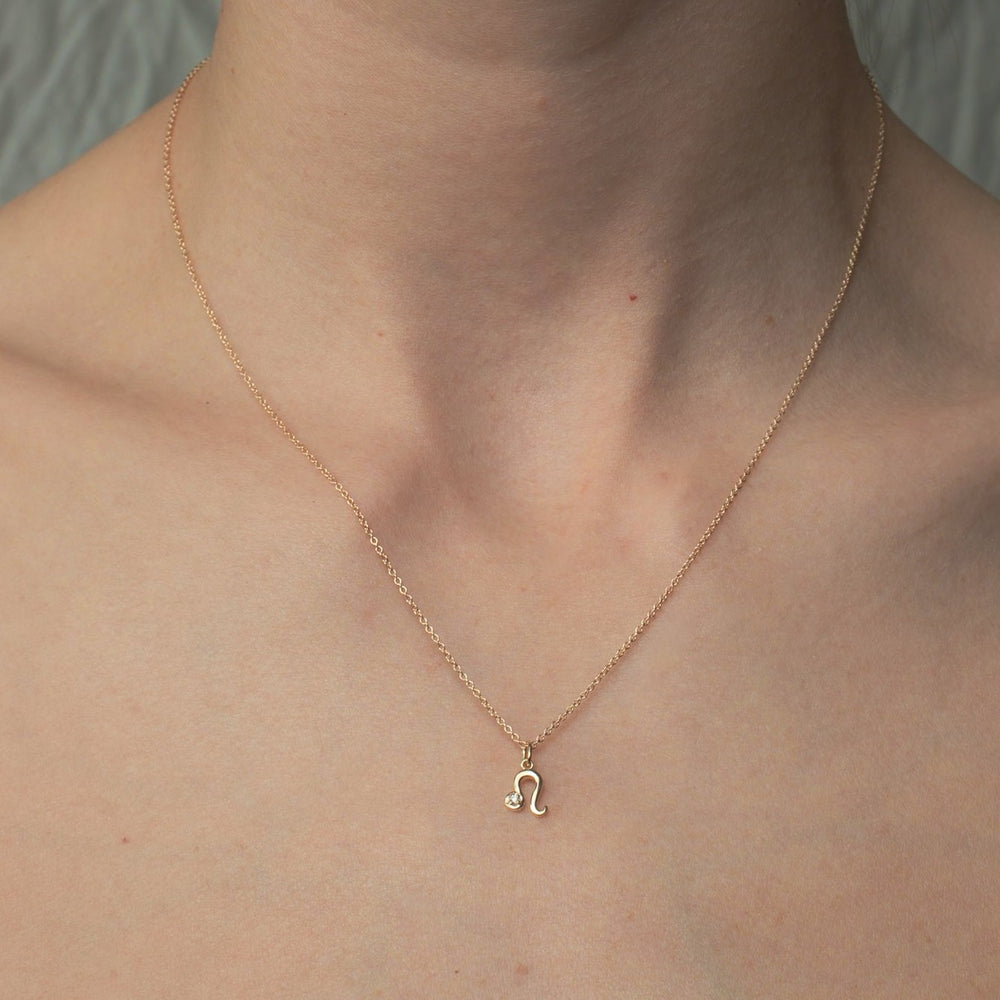 
                      
                        A close-up image showcases a person's neck adorned with the Pear Diamond Zodiac Necklace—a delicate gold chain featuring a small diamond pendant in the shape of the Leo zodiac symbol. The adjustable cable chain enhances its versatility, set against a plain and neutral background.
                      
                    