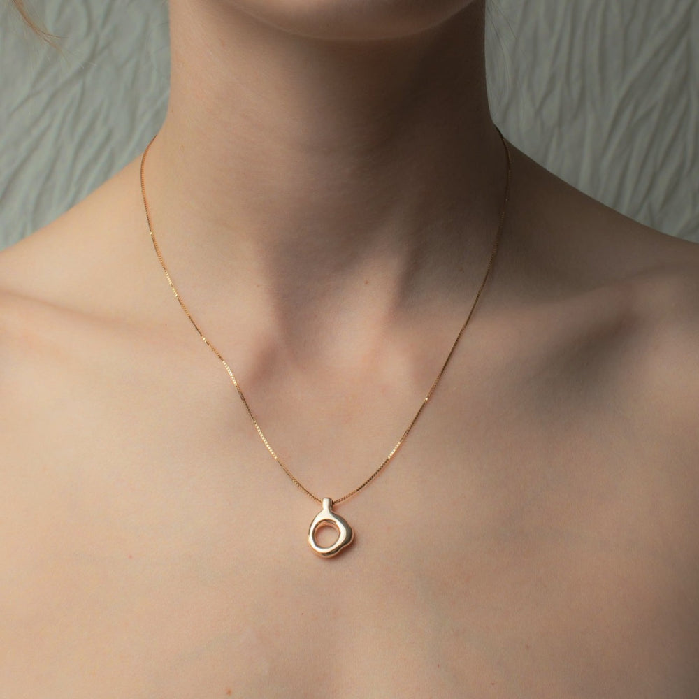 
                      
                        A close-up of a woman's neck and collarbone featuring the Pear Odette Necklace, an elegant piece of timeless jewelry. The solid gold pendant boasts a polished circular frame with an irregular, organic shape. The softly textured background adds depth to the minimalist composition.
                      
                    