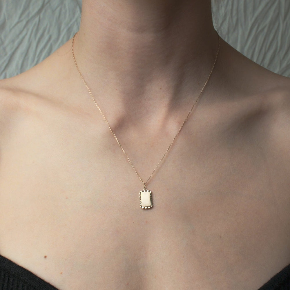 
                      
                        A close-up photo of a person's neck and upper chest showcases the Pear Engraveable Rectangle Necklace, a thin, gold piece featuring an engravable rectangular pendant. The person is wearing a black, off-the-shoulder top against a textured, light-colored background. The adjustable cable chain adds versatility to this elegant jewelry item.
                      
                    