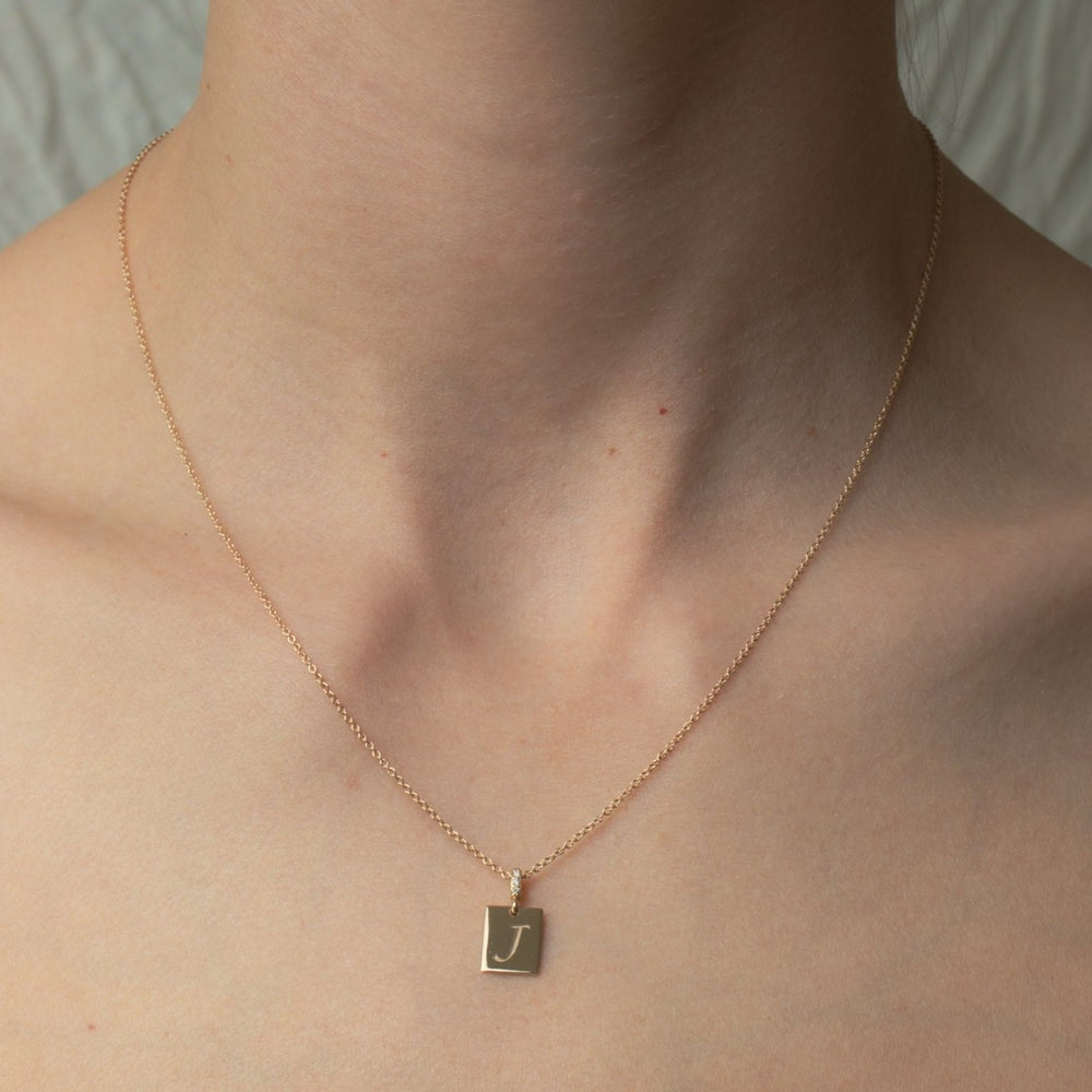 
                      
                        A close-up image of a person wearing the Diamond Cleo Initial Necklace by Pear, featuring a delicate gold chain with a small, customizable pendant hanging in the center. The pendant displays the letter "J" engraved on it. The person's bare neck and partial collarbone are visible against a neutral background, showcasing this versatile accessory.
                      
                    