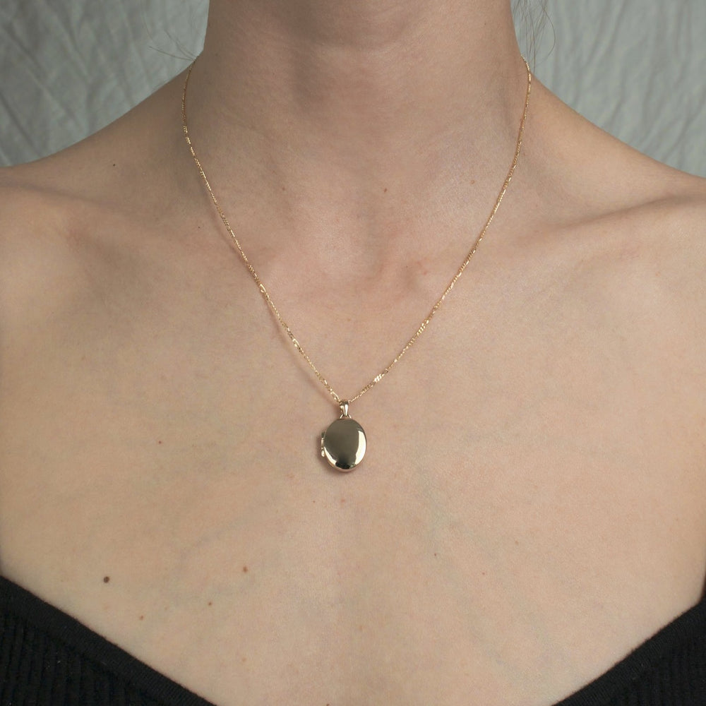 
                      
                        A person wearing a delicate Pear Oval Locket made of 14K gold with a shiny pendant. The background is neutral, and the person is dressed in a black, off-the-shoulder top.
                      
                    