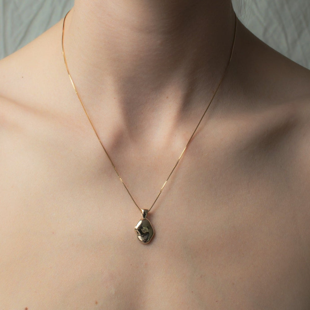 
                      
                        An intimate close-up captures a person's neck graced by the Ophelia Necklace from Pear, a delicate solid gold chain featuring a uniquely, hand-carved oval pendant. The softly blurred background enhances focus on this exquisite piece of jewelry.
                      
                    