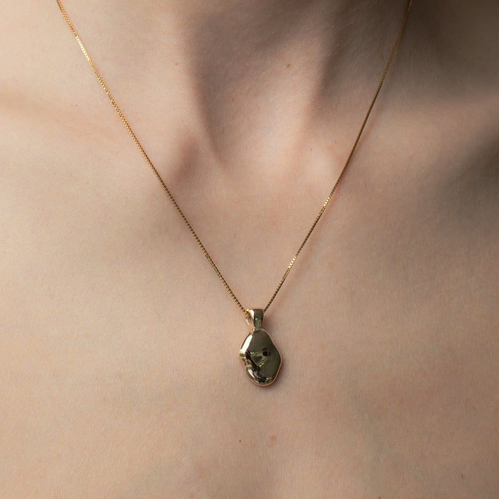 
                      
                        A close-up image reveals a light-toned neck adorned with the Ophelia Necklace by Pear, featuring a delicate gold chain. The hand-carved oval pendant, inspired by Ophelia's grace, boasts an irregular, organic shape and a shiny finish, resting elegantly just above the collarbone.
                      
                    