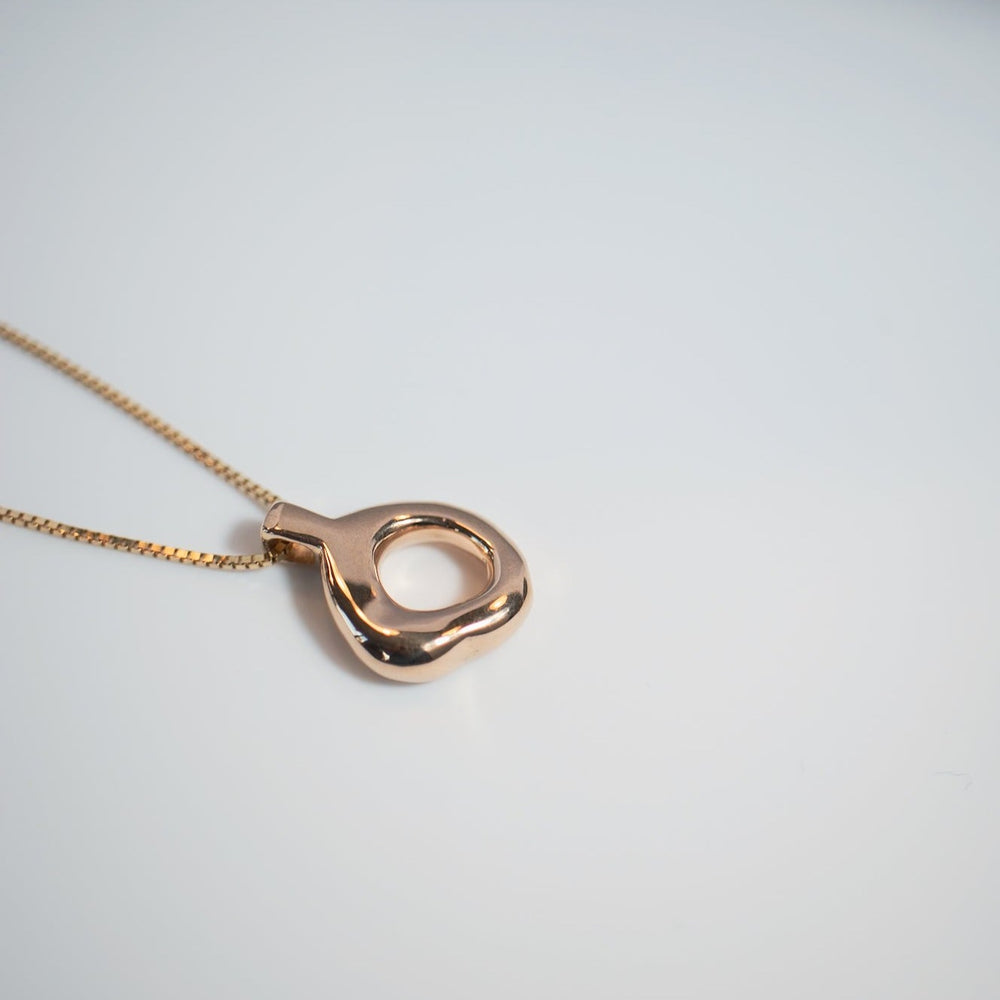 
                      
                        A close-up of the Odette Necklace by Pear., showcasing a polished, modern pendant with a loop design. The solid gold pendant and chain are set against a plain, light background, emphasizing the elegant simplicity of this timeless jewelry piece.
                      
                    