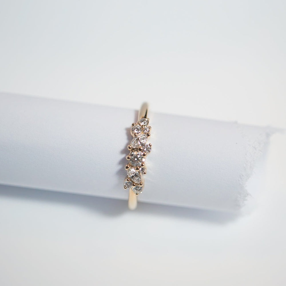 The Celeste Diamond Ring by Pear, a delicate 14K gold piece adorned with a cluster of small, sparkling diamonds, is elegantly wrapped around a white cylindrical object on a white background. Its minimalist design enhances both the ring's elegance and the brilliance of the diamonds.