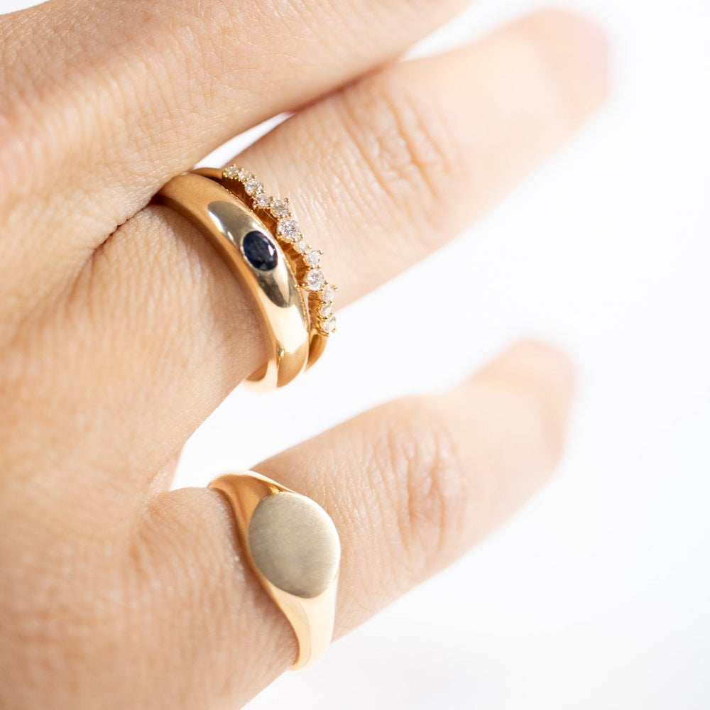 
                      
                        Close-up view of a hand adorned with three gold rings from Pear jewelry. The top ring features a row of small gemstones, the middle ring is the stunning Sapphire Dome Ring showcasing a dark blue Sapphire set in the center, and the bottom ring is a sleek 14K gold signet band. The white and blurred background enhances the elegance of these exquisite pieces.
                      
                    