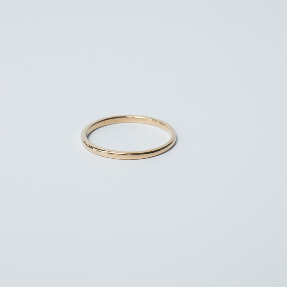 The Round Band by Pear is a simple, thin, solid gold ring set against a plain light background. This smooth and unadorned round band perfectly embodies minimalist design, making it a timeless piece.