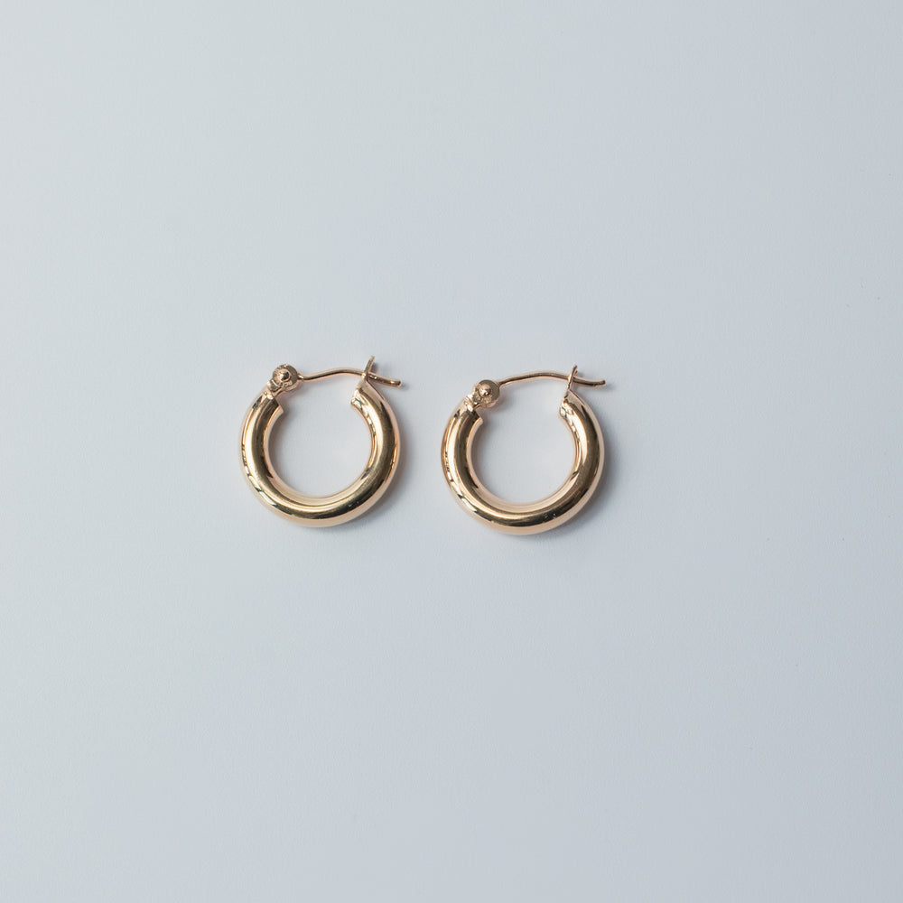 
                      
                        The Mini Thick Hoops by Pear, a pair of small 14K gold hoop earrings, are elegantly displayed on a light gray background. These mini hoops feature a plain, smooth, polished surface and latch backs for secure closure. Their simplicity and shine make them perfect for everyday wear, standing out beautifully against the neutral backdrop.
                      
                    