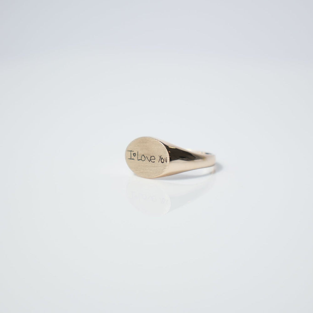 
                      
                        A Handwritten Oval Signet Ring from Pear. sits on a reflective white surface, showcasing a laser-engraved message that says "I Love You." The plain white background enhances its minimalist and elegant appeal. Customize this ring to make it uniquely yours.
                      
                    