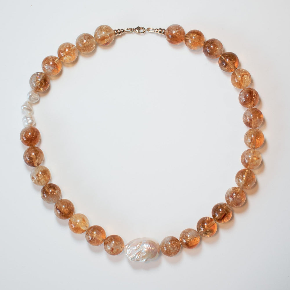 The Citrine and Pearl Beaded Necklace by Pear. elegantly rests in a circle on a white background, showcasing its translucent amber-colored beads and captivating baroque pearl centerpiece.