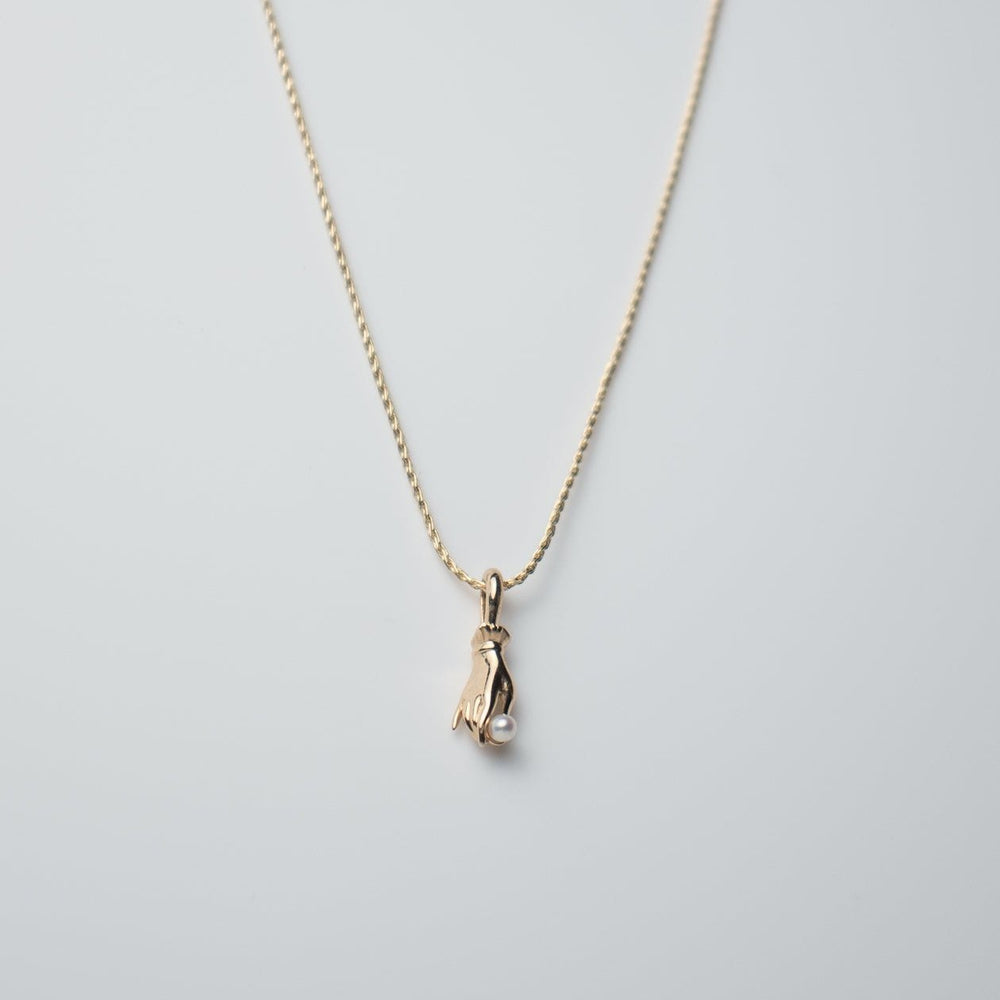 The elegant Pearl Buddha Hand Necklace by Pear. showcases a minimalist design in 14K yellow gold, featuring a penguin-shaped pendant set against a light gray background, adding an exquisite touch to the simple chain.