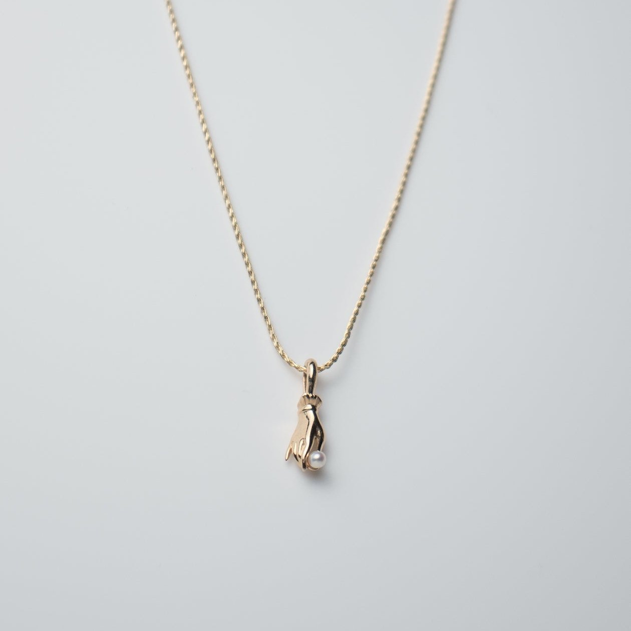 The elegant Pearl Buddha Hand Necklace by Pear. showcases a minimalist design in 14K yellow gold, featuring a penguin-shaped pendant set against a light gray background, adding an exquisite touch to the simple chain.