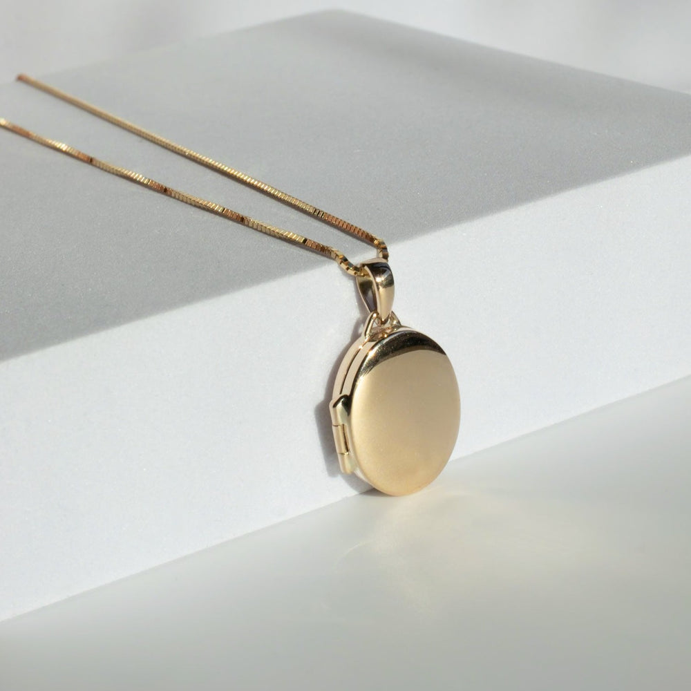 
                      
                        A close-up image of Pear's Oval Locket pendant on a delicate 14K gold chain. The locket, featuring a smooth, oval surface, is placed on a minimalist white background. The thin chain complements the locket's elegant design, exuding sophistication and simplicity.
                      
                    