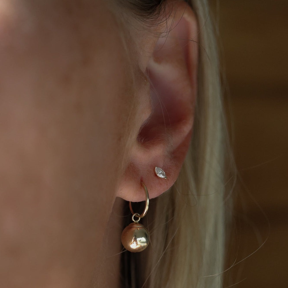 
                      
                        Close-up of an ear showcasing two earrings: a small, marquise-cut diamond stud in the upper lobe and Pear's Endless Baby Hoop with Dangle in 14K Yellow Gold on the lower lobe. The background is softly blurred.
                      
                    