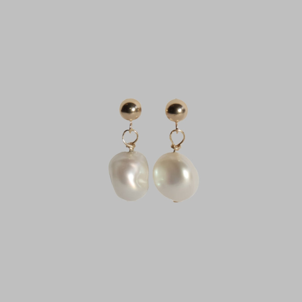 
                      
                        Introducing the Pearl Boule Earrings by Pear: a pair of elegant earrings showcasing round 14K gold balls at the top, from which white, irregularly shaped freshwater pearls gracefully dangle. The solid light gray background enhances the simple yet sophisticated design of these exquisite earrings.
                      
                    