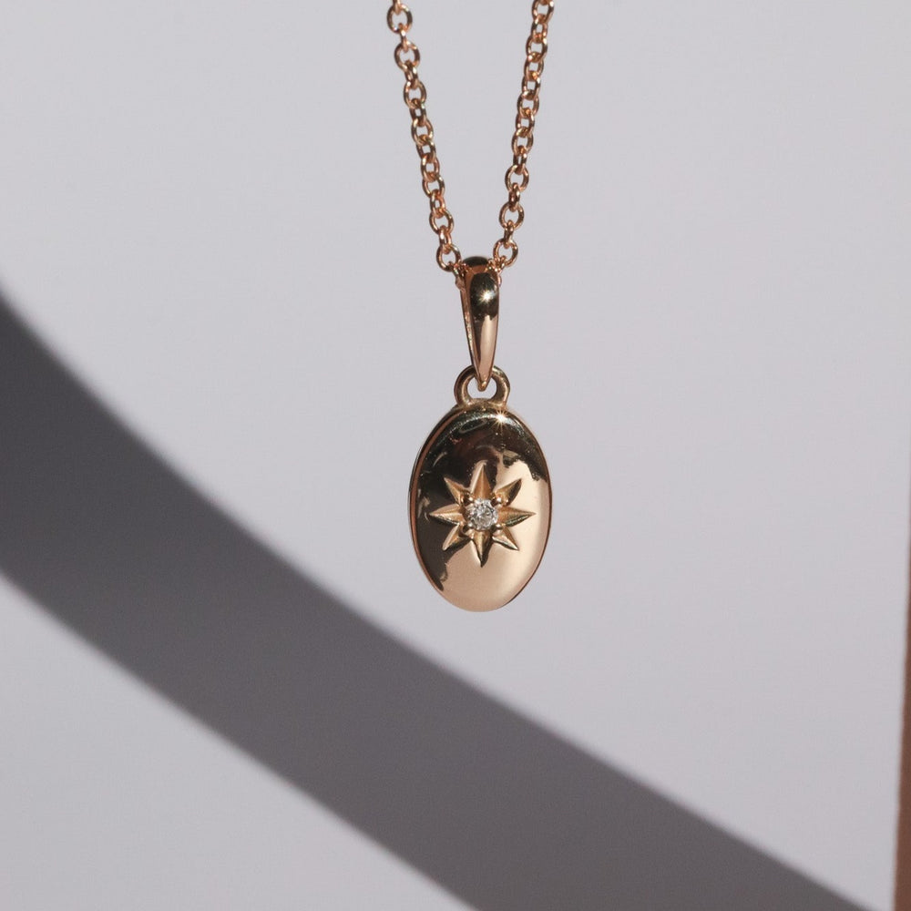 
                      
                        The Astrid Necklace by Pear is a gold necklace featuring a circular 14k gold pendant with a starburst design and a small diamond at its center. The pendant gracefully hangs from a delicate chain against a plain light grey background, with a soft shadow cast behind it.
                      
                    