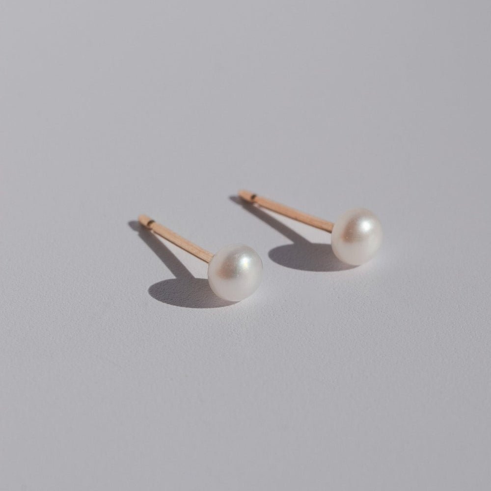 
                      
                        A pair of elegant Pearl Studs from Pear with 14K gold posts rest on a light gray surface. The round, lustrous pearls cast subtle shadows, exuding timeless sophistication.
                      
                    