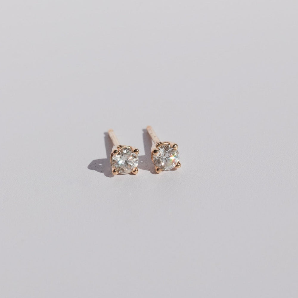 
                      
                        The Diamond Prong Studs by Pear feature round, natural brilliant cut diamonds set in gold prongs. Positioned side by side on a plain, light-colored surface, the earrings highlight their minimalist design and diamonds of SI1 grading quality.
                      
                    