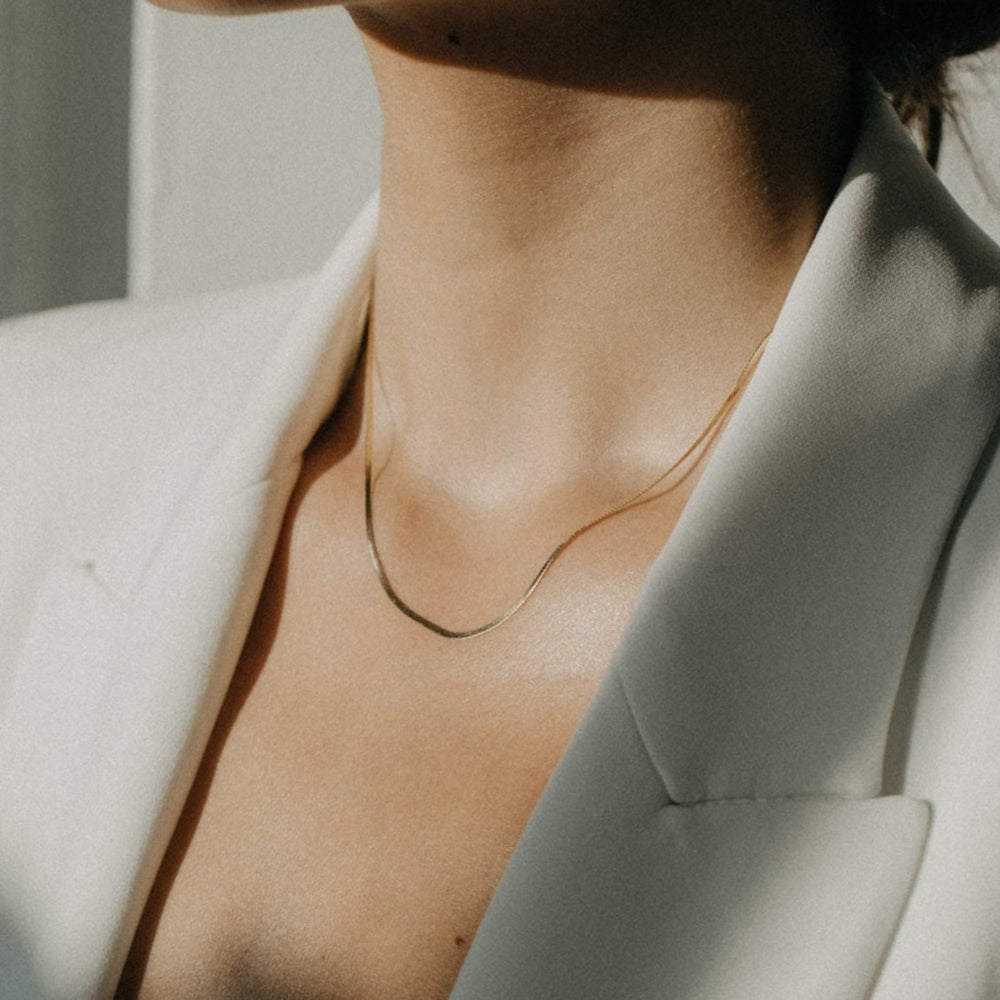 
                      
                        A close-up of a person wearing Pear's delicate 14K gold Thin Herringbone Chain and a white blazer. The background is softly lit, creating a minimalist and elegant atmosphere.
                      
                    