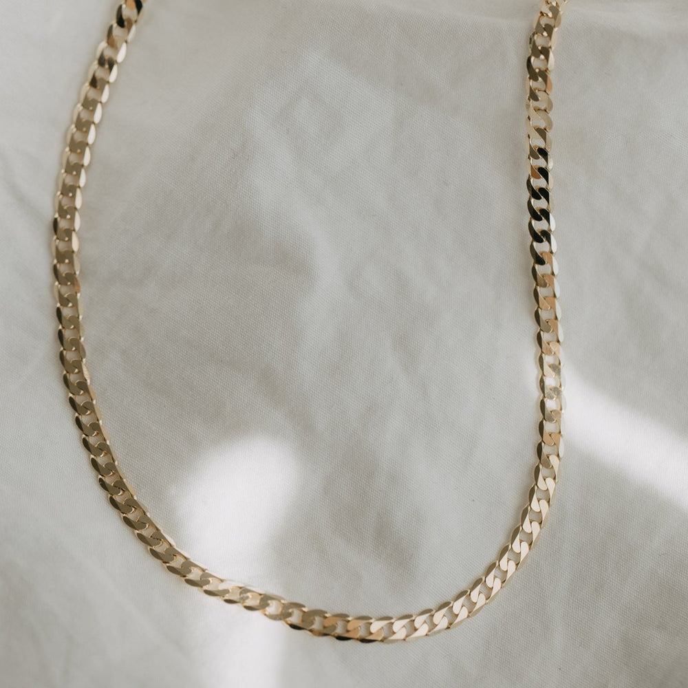 
                      
                        The Pear Curb Chain Necklace laid flat on a soft, textured white cloth background showcases its 14K Solid Yellow Gold construction. The polished and reflective surface of the chain creates subtle light glints, emphasizing its minimalist elegance. Designed for daily wearability, this piece ensures both comfort and style.
                      
                    