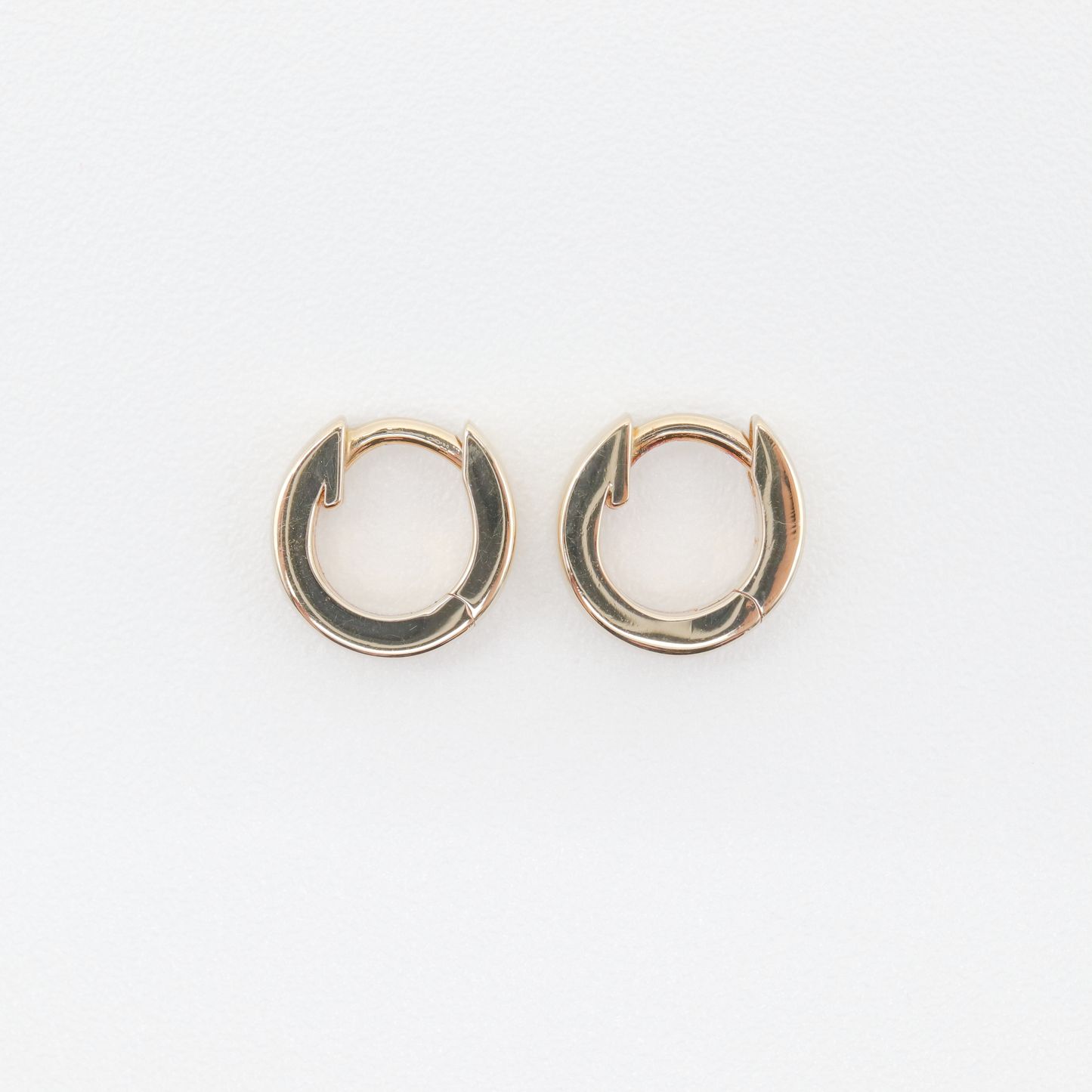 A pair of small, 14k gold huggie earrings from Pear. Known as The Huggies, these hoops feature a smooth, shiny finish with a simple and elegant design set against a white background.