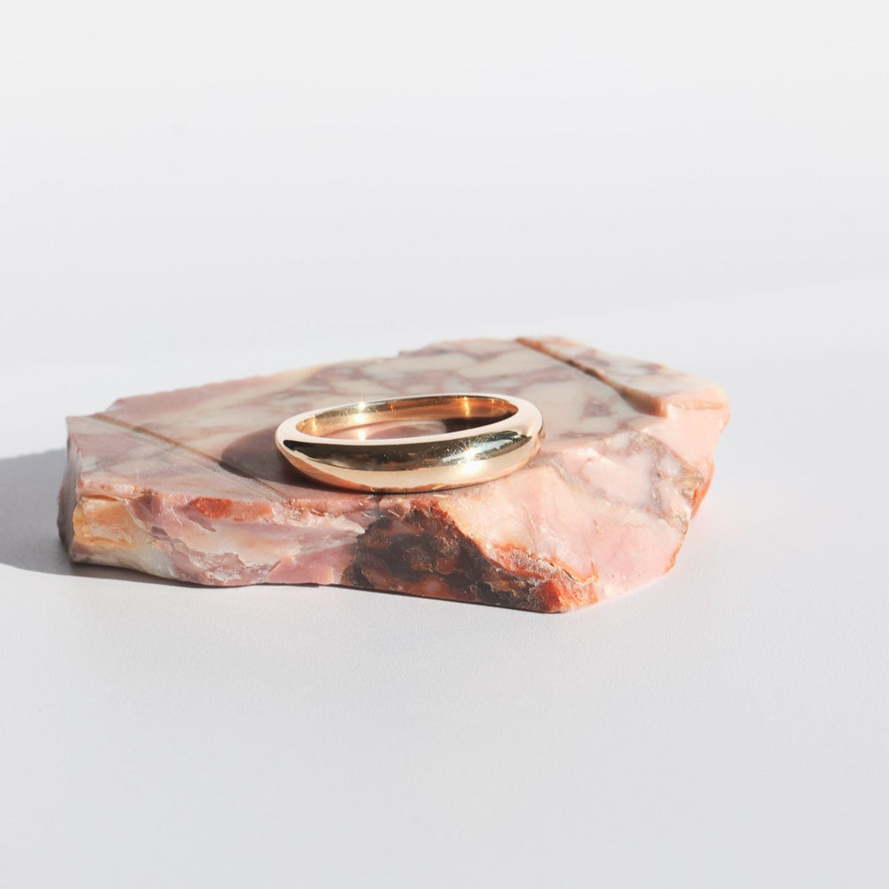 
                      
                        The Dome Ring by Pear, crafted from 14K Yellow Gold with a sleek and smooth surface, is elegantly positioned on a polished pink and white marble slab. The plain white background accentuates the simplicity and elegance of this daily layering jewelry piece on its natural stone base.
                      
                    