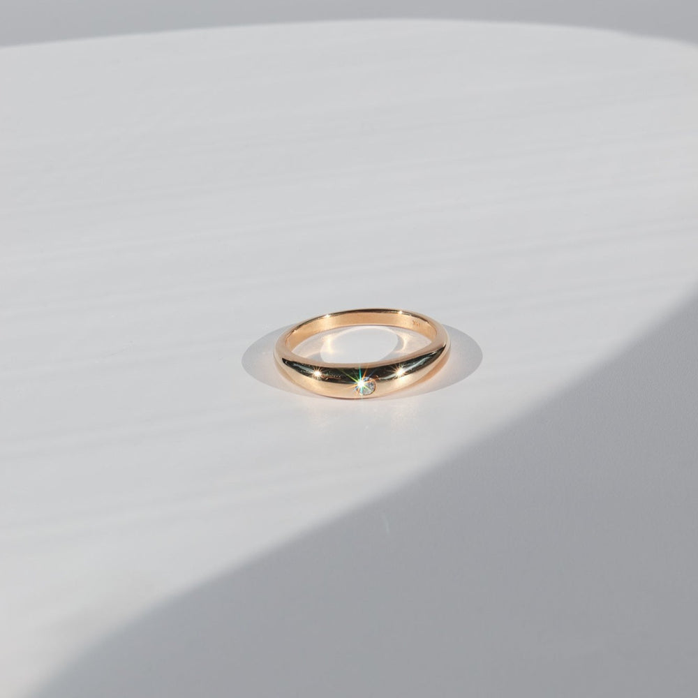 
                      
                        The Diamond Dome Ring by Pear, featuring a solid gold dome design with a 2mm diamond, is placed on a white surface. Soft shadows fall around it, accentuating its simplicity and elegance.
                      
                    