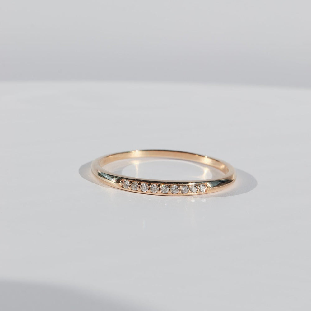 
                      
                        An Esme Diamond Ring by Pear, featuring a delicate gold band with petite diamonds adorning the top section, is set on a smooth, light-hued surface against an unadorned background. The ring's shadow softly accentuates its graceful and minimalist design.
                      
                    